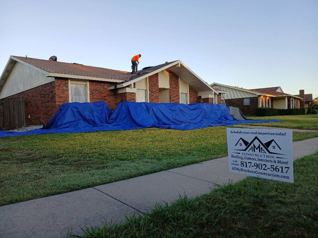 Roofing work in progress on a home with blue tarps and a construction sign in the front yard.