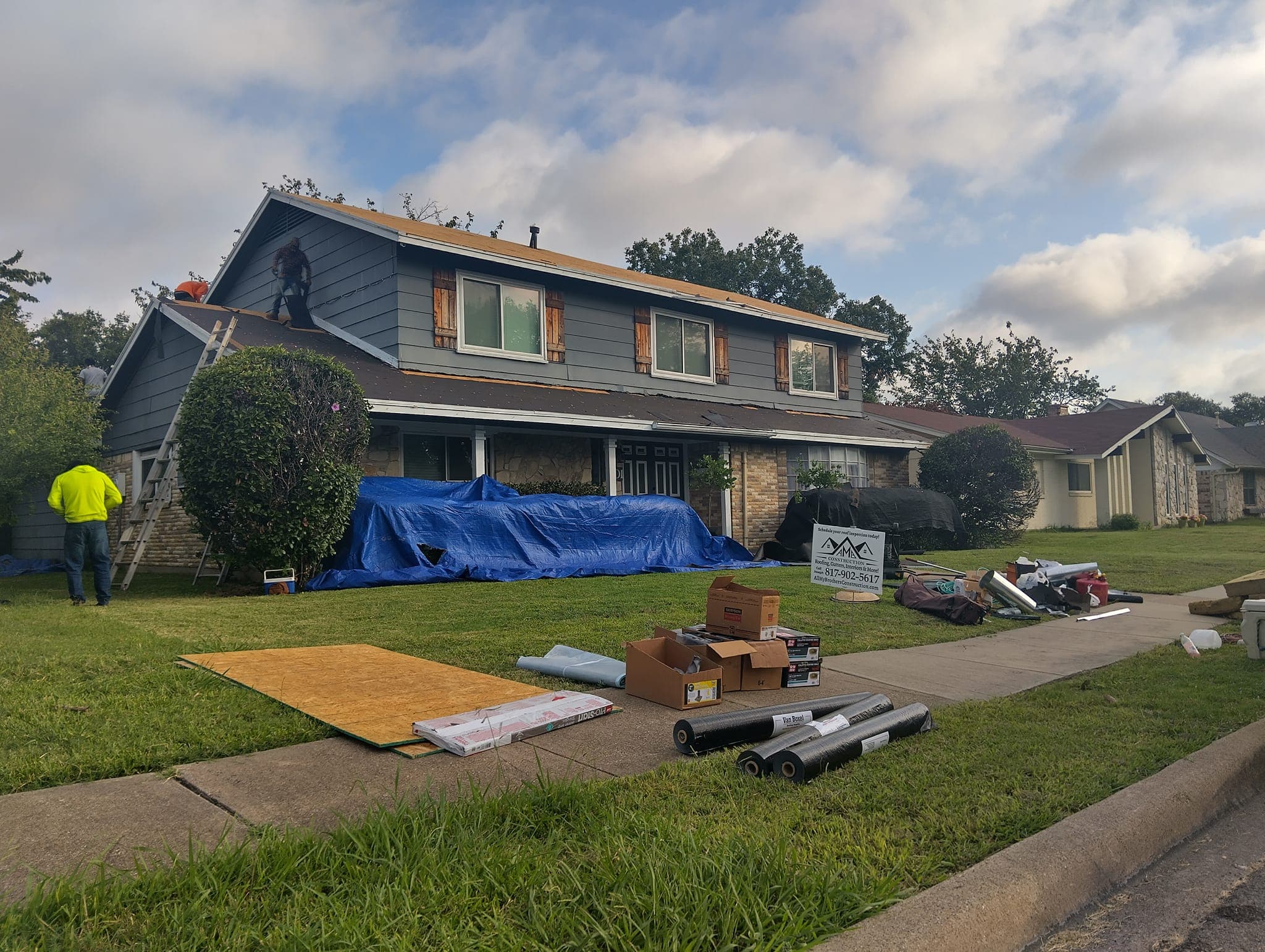 Roofing project in progress on suburban home with construction materials and tarp outdoors.