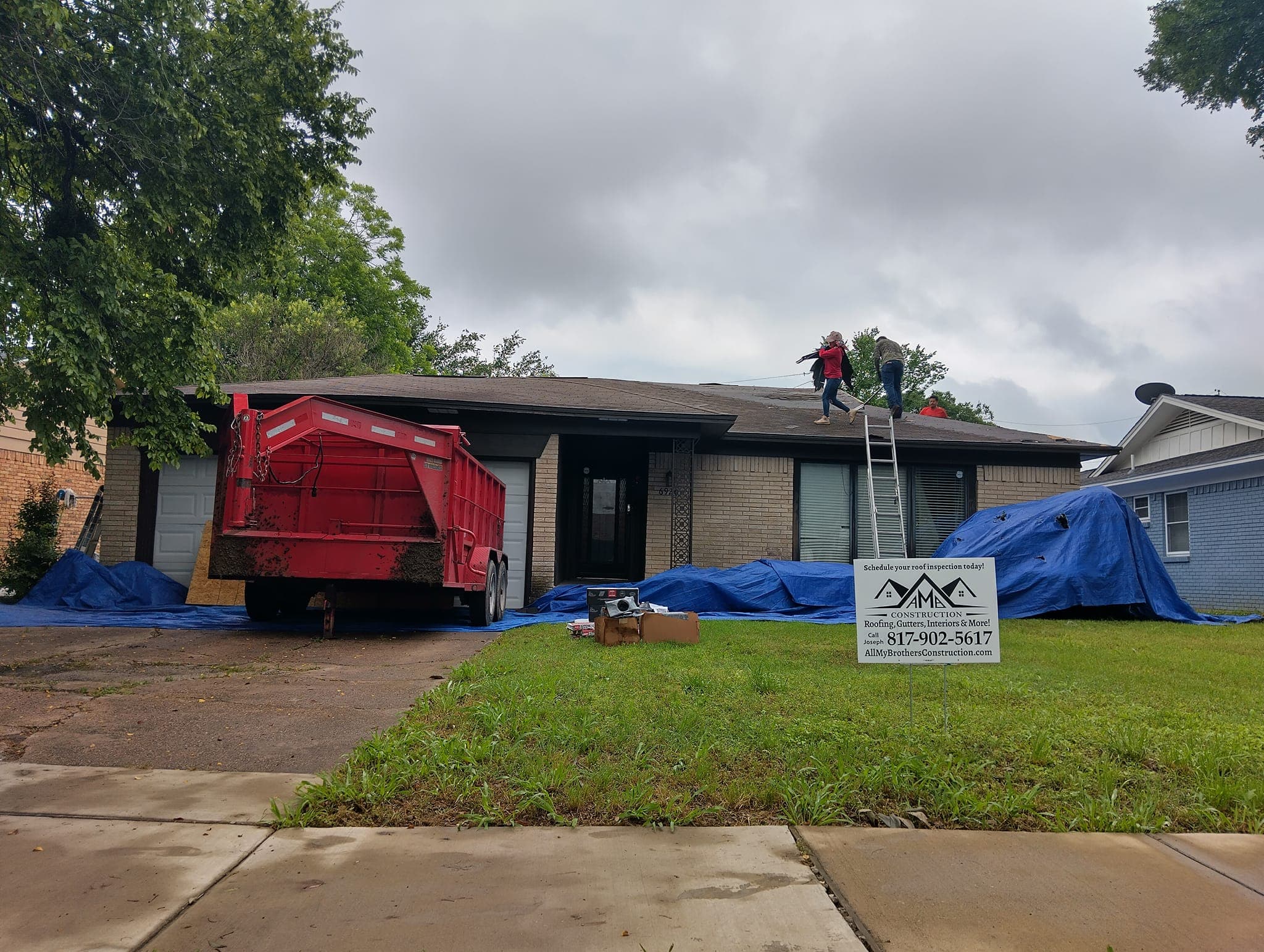 Roof repair in progress on residential home with workers on scaffolding, debris container in driveway.