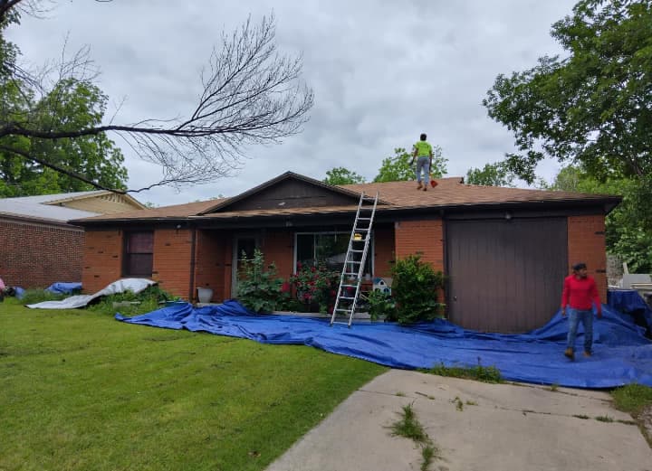 Roof renovation in progress on a suburban home, with workers and blue tarps visible.